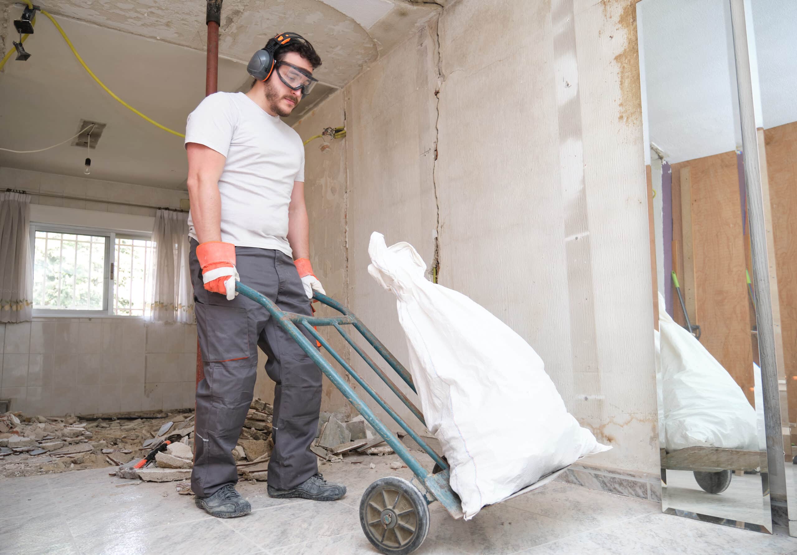 Builder collecting construction debris in a bag, and carrying in a hand trolley. House renovation.